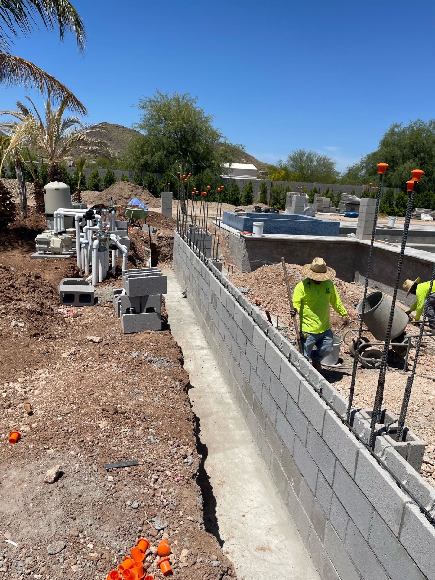 Aurora Estate — long block wall under construction with the pool equipment skid, plumbing manifold, and desert mountain backdrop visible beyond